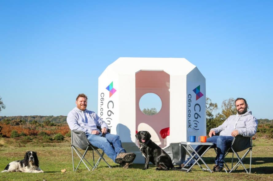 two people and dog sitting in lawn chairs outside a small white pod